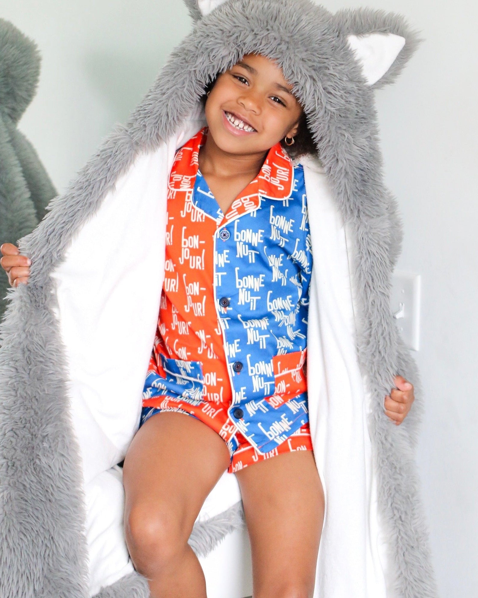 Child wearing a long gray hood with animal ears, standing against a white background.