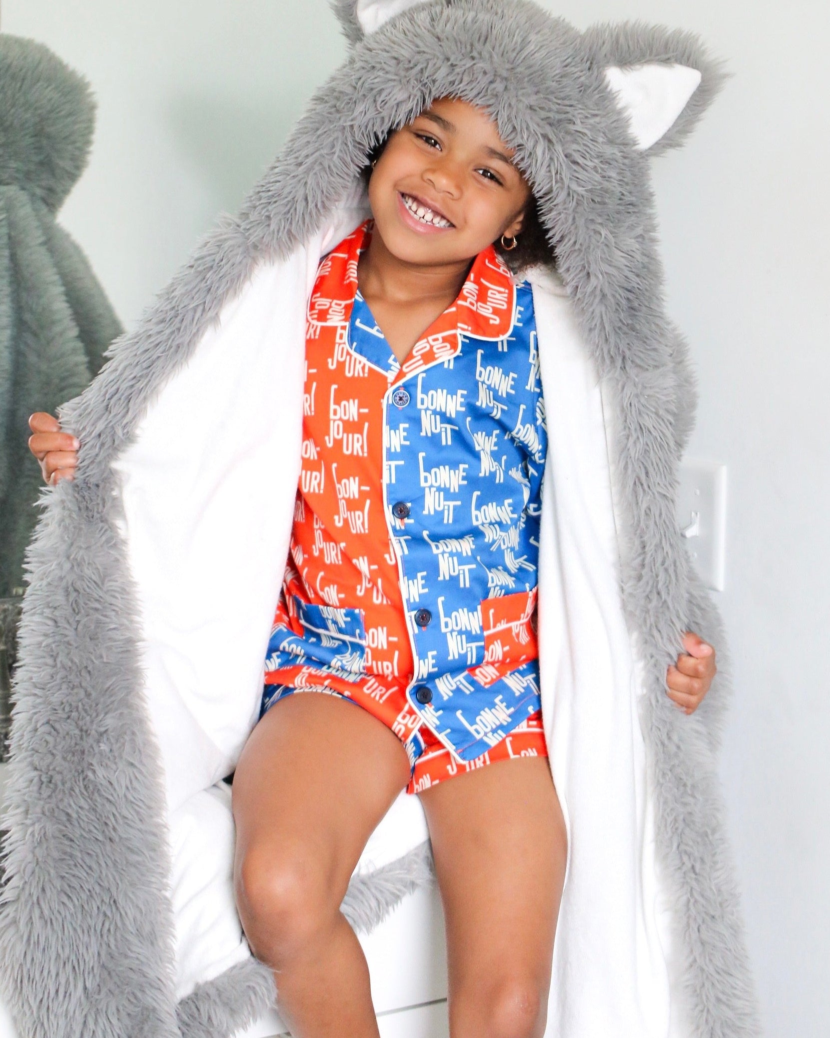 Child wearing a long gray hood with animal ears, standing against a white background.