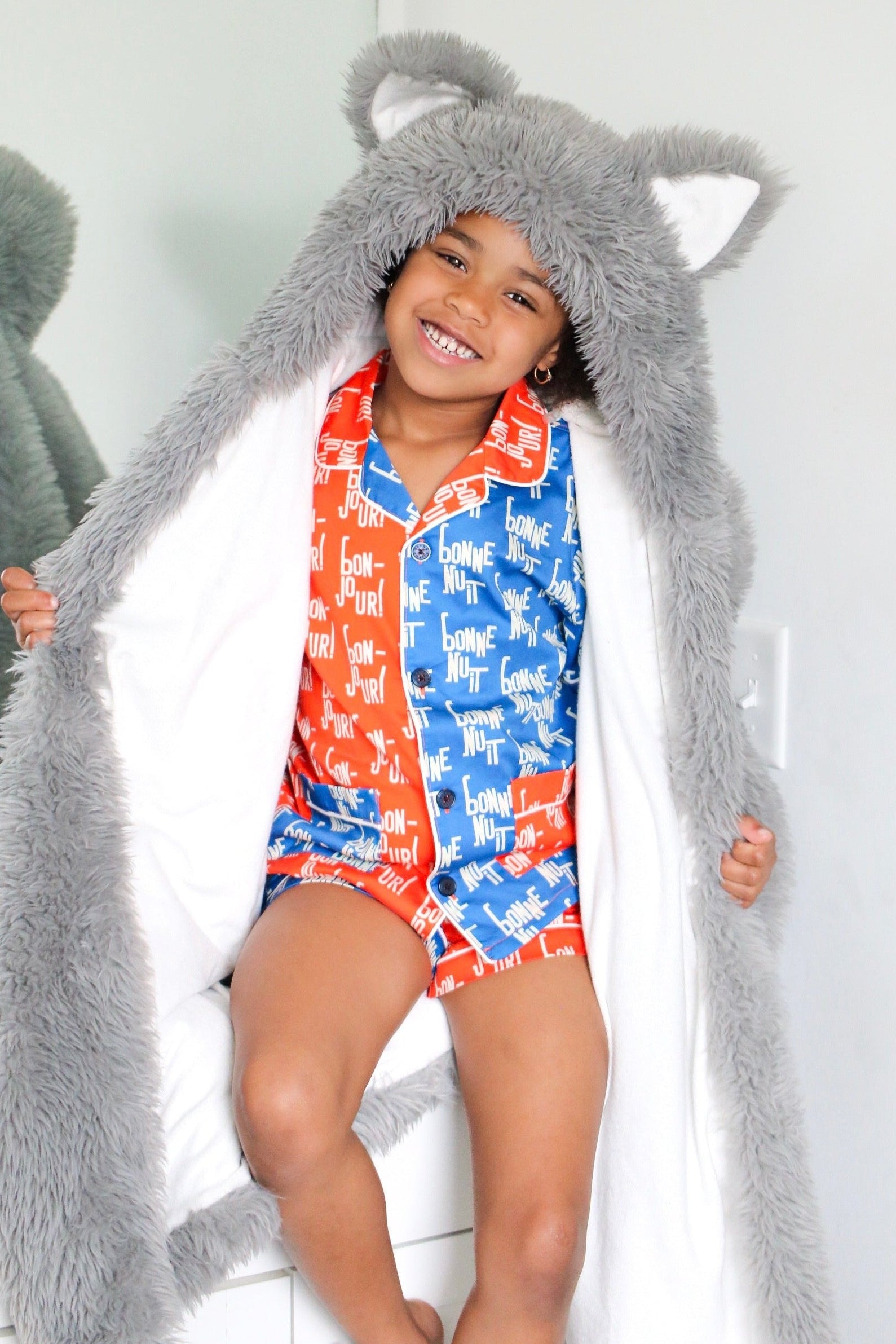 Child wearing a long gray hood with animal ears, standing against a white background.
